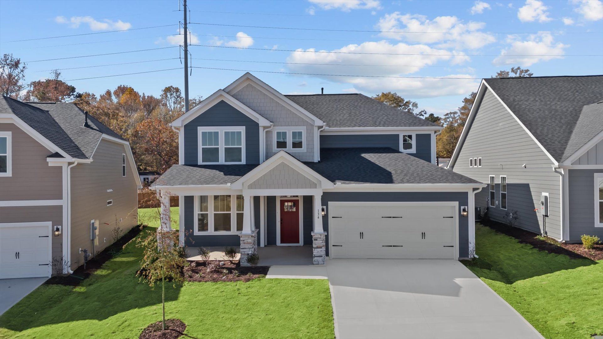 Stunning shot of dark blue exterior home with two car garage, stone columns, and front porch at Pelham Crossing by DRB Homes