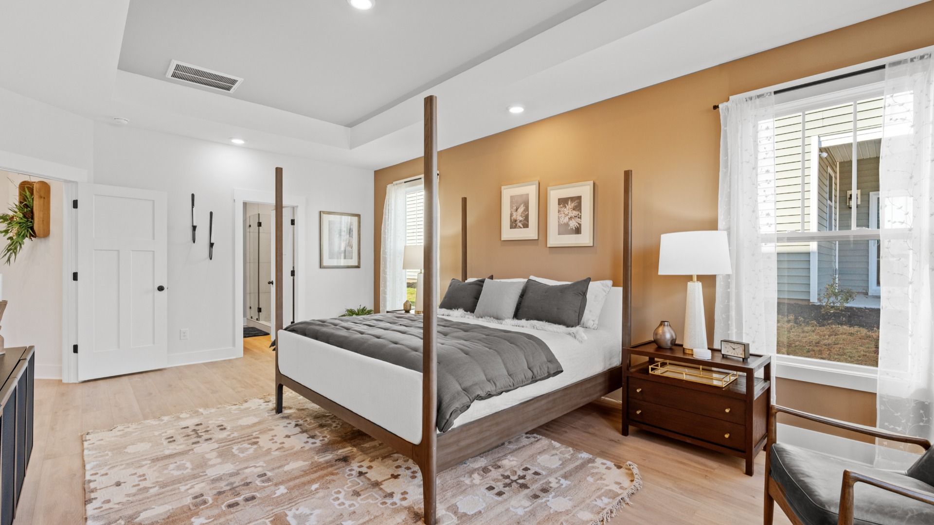 Elegant primary suite with hardwood flooring, tray ceiling, and superior natural light in this accomplished DRB Homes design