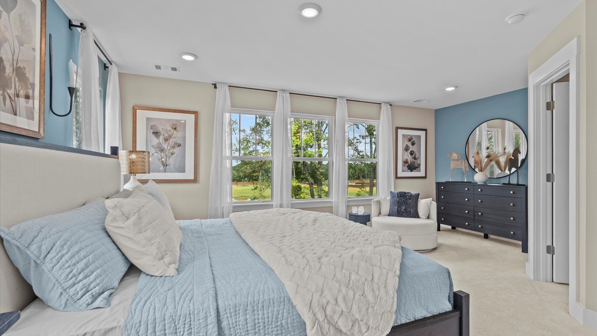 Plush carpeted primary suite with accent wall and ceiling fan in two story townhome at Saluda Crossing by DRB Homes
