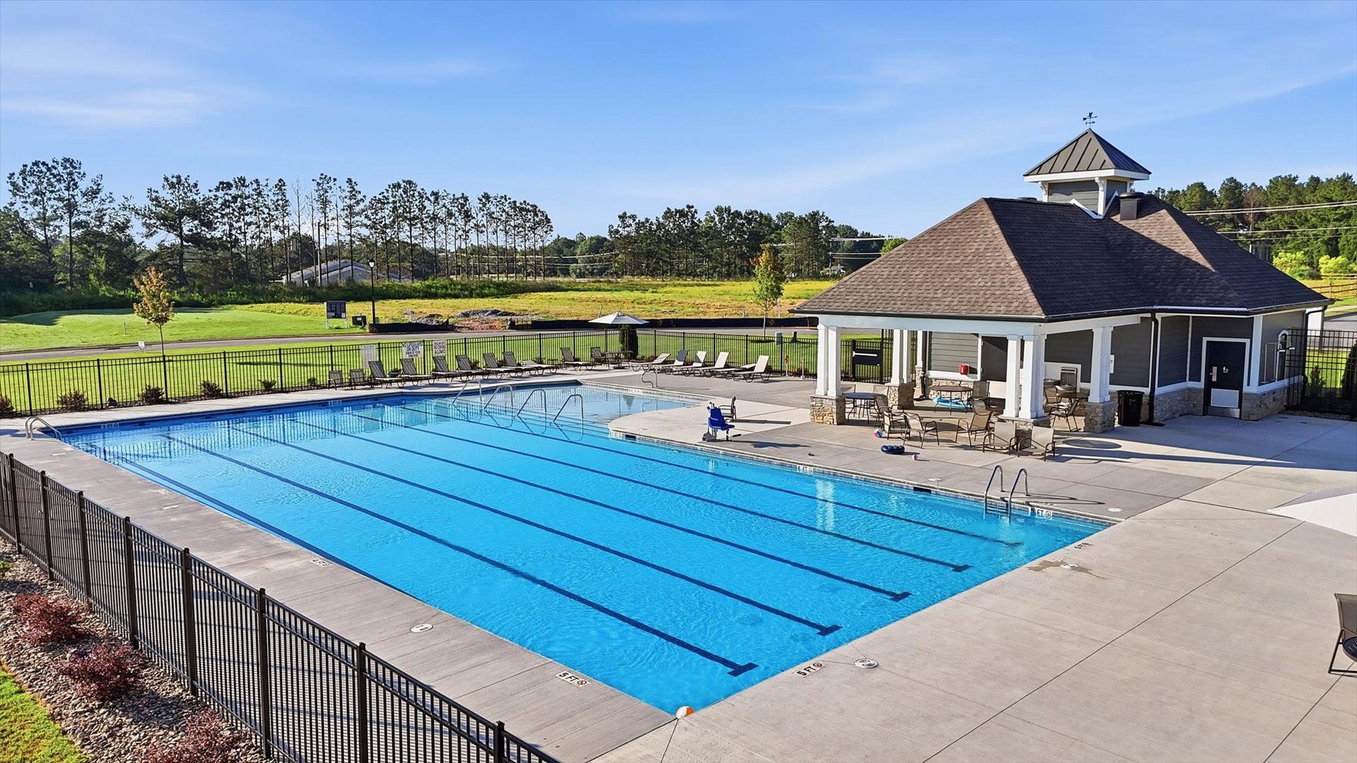 Eye-catching community pool with landscaped greenery, community clubhouse, and outside seating