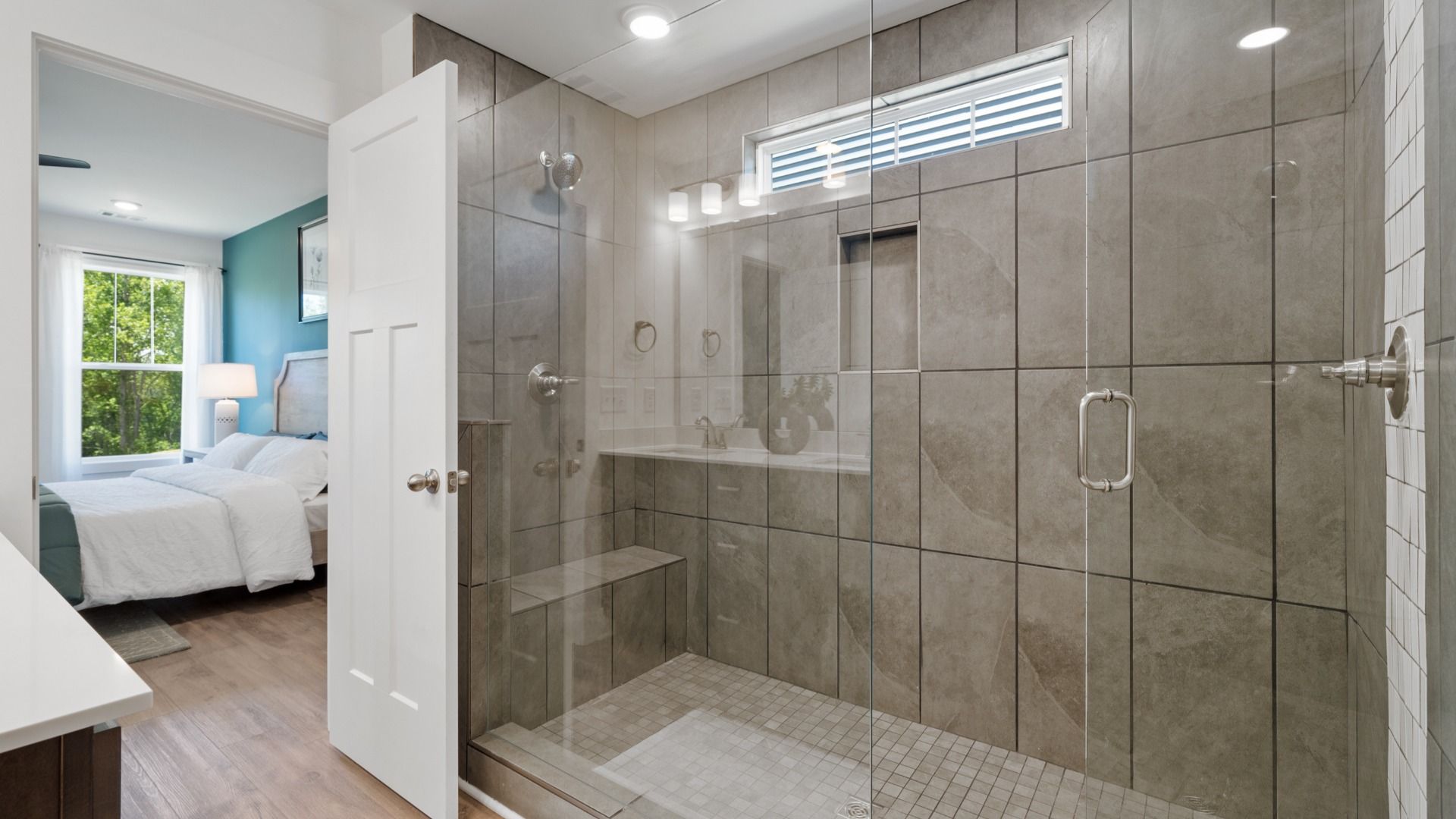 Tiled Roman walk-in shower with netural large tiles and frameless glass doors at Magnolia Park by DRB Homes in Woodruff, SC