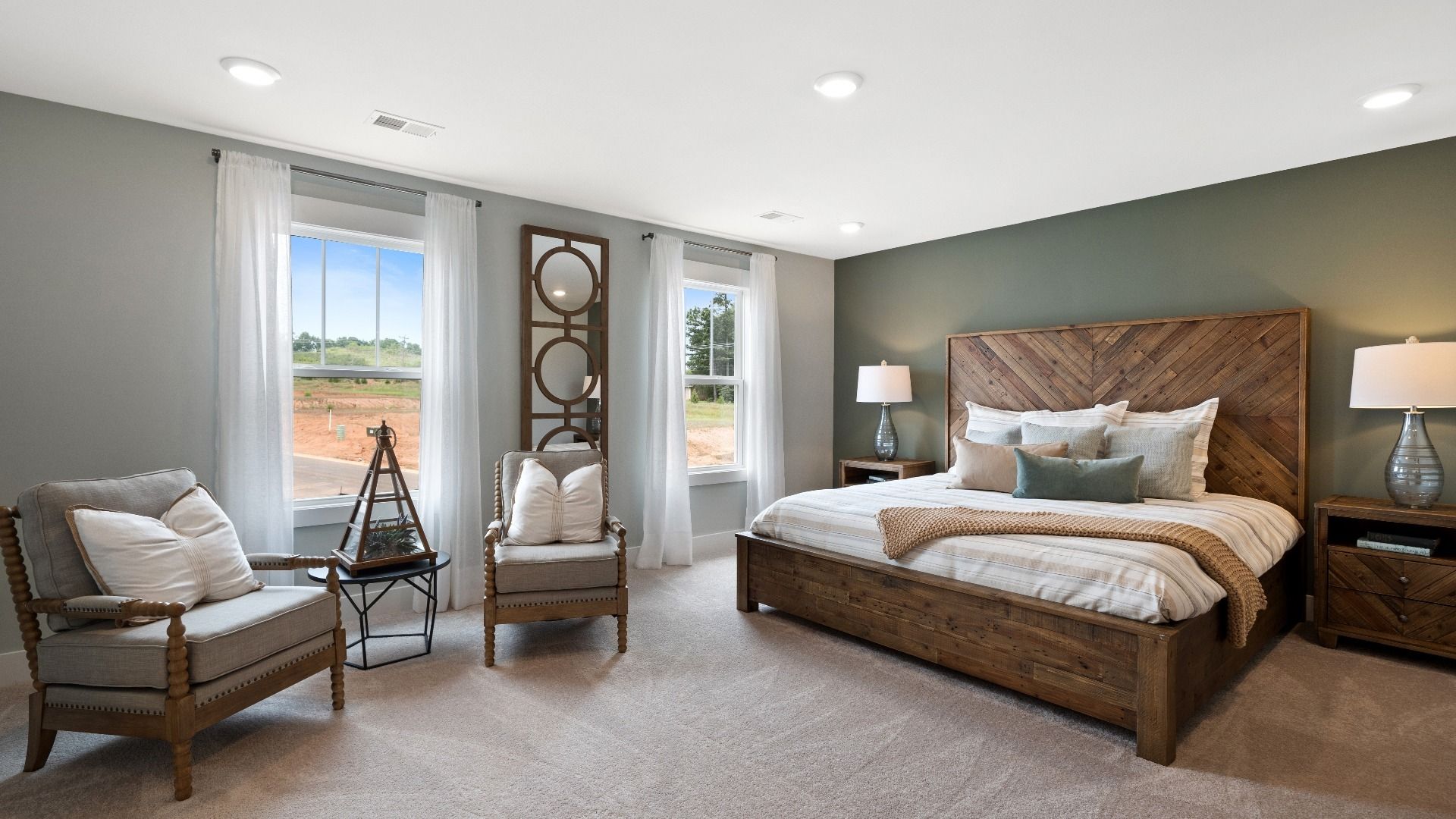 Plush carpeted primary suite with green accent wall, large windows, and overhead lighting at Walnut Ridge by DRB Homes