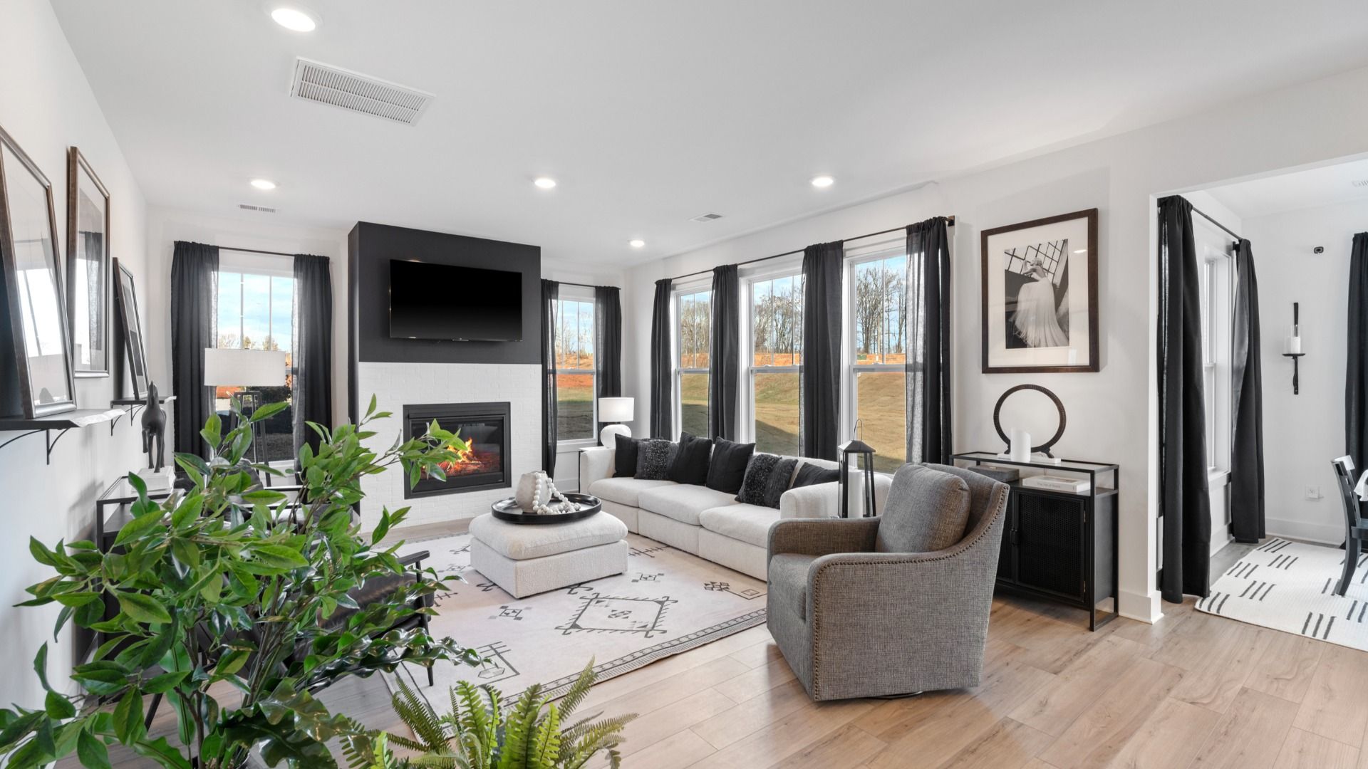 Modern family room with boasting windows, black and white fireplace, and warm toned hardwood flooring in Spartanburg, SC