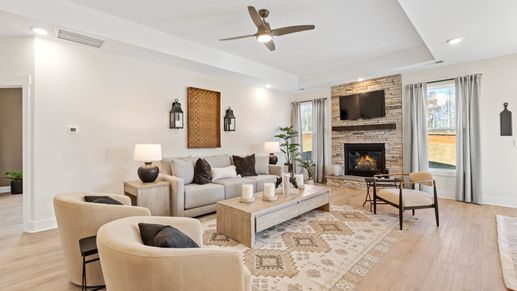 Cozy, inviting family room with stone fireplace, vaulted ceiling, overhead fan, and LVP flooring at Fox Hollow by DRB Homes