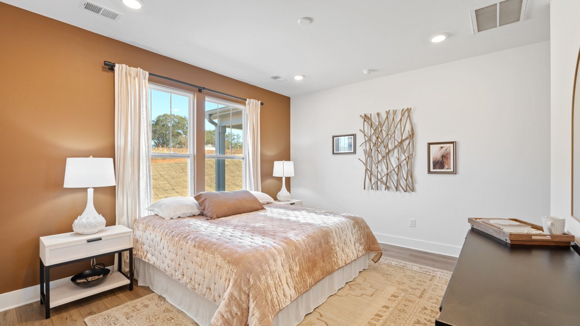 Large windows and hardwood flooring elevate this owner's suite to the next level, plus a warm toned accent wall
