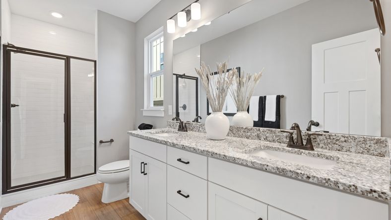 Primary bathroom with modern black hardware, tiled walk in shower, and double sink vanity with granite countertops