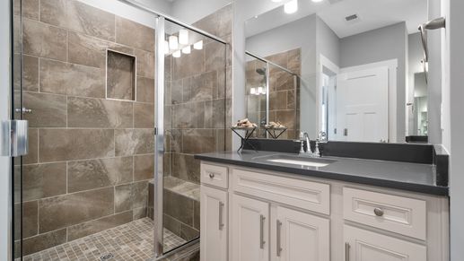 Primary suite with dark tile shower, white cabinets, and quartz countertops at Village at Midway by DRB Homes in Anderson, SC