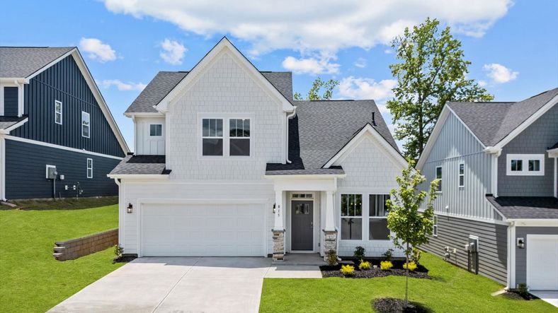 Bright white exterior home with gray door and stone details at Pleasant Falls by DRB Homes in Moore, SC