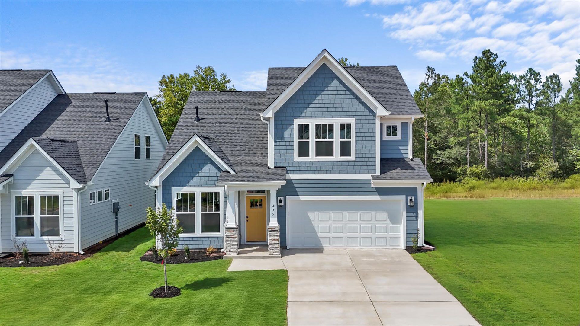 Ocean blue exterior home with popping yellow front door, stone detailed columns, and two car garage in Moore, SC
