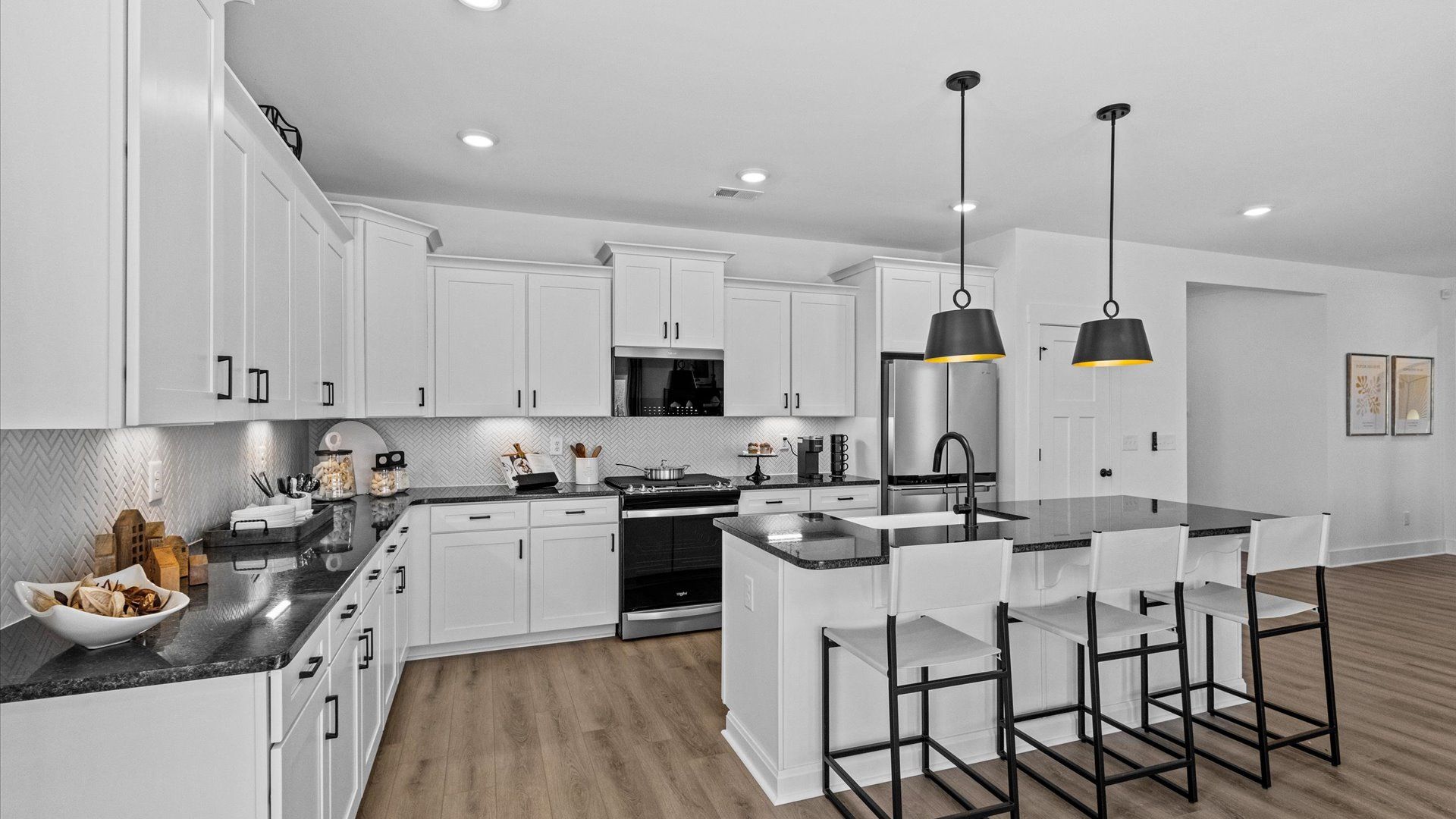 Large kitchen with black accents and white cabinetry with large island with counterstools at Wells Crossing by DRB Homes