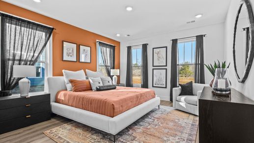 Modern, orange accented primary suite with large windows and hardwood flooring with elevated ceilings at Wells Crossing
