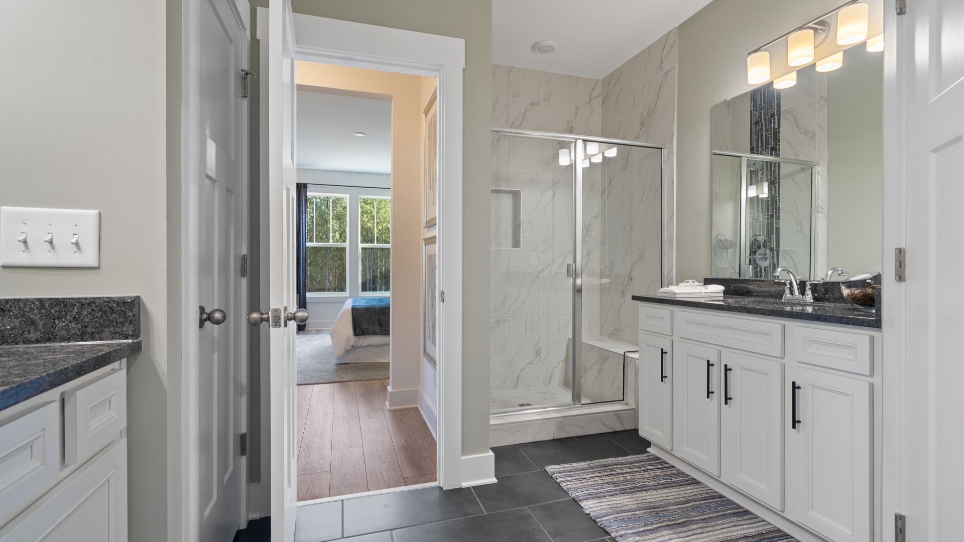 Primary suite with dark tile flooring, white tile shower, separate vanities with dark countertops and white cabinets