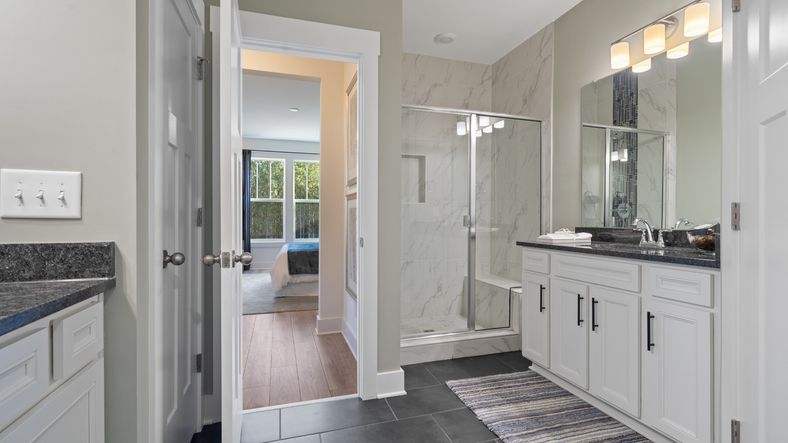 Primary suite with dark tile flooring, white tile shower, separate vanities with dark countertops and white cabinets