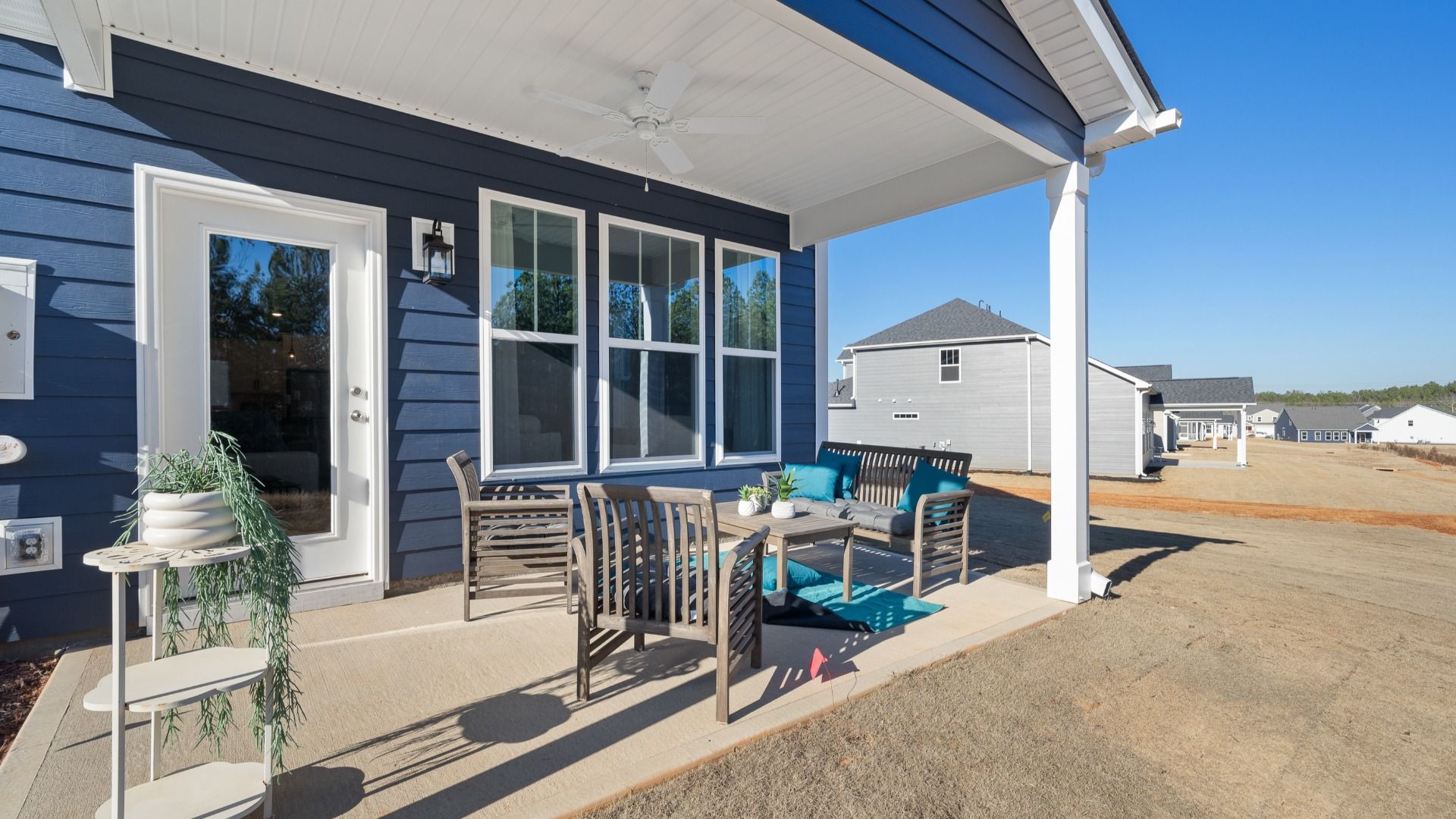 Dark blue exterior home with covered back porch with ceiling fan and patio furniture set at Village at Midway by DRB Homes