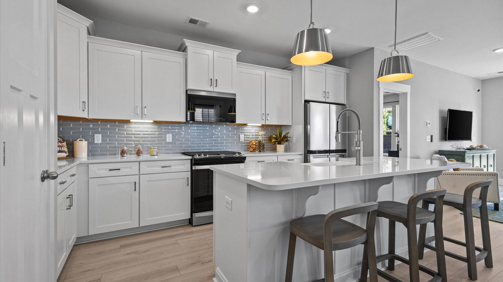 Large kitchen with white cabinetry, gray backsplash, and large island with room for counter stools at Pleasant Falls
