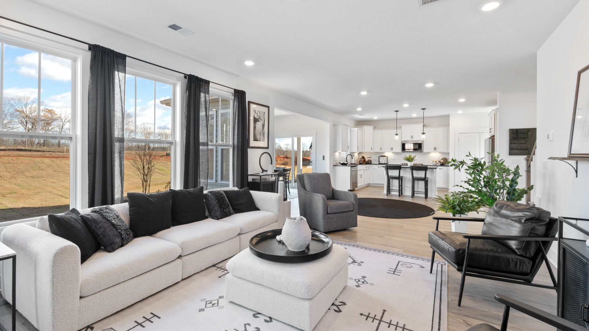 Modern family room with hardwood flooring, elevated ceilings, and black and white decor at Fox Hollow by DRB Homes