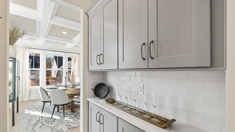Butler's Pantry with grey cabinetry on top and bottom, white brick backsplash, and bar set up at Fox Hollow by DRB Homes