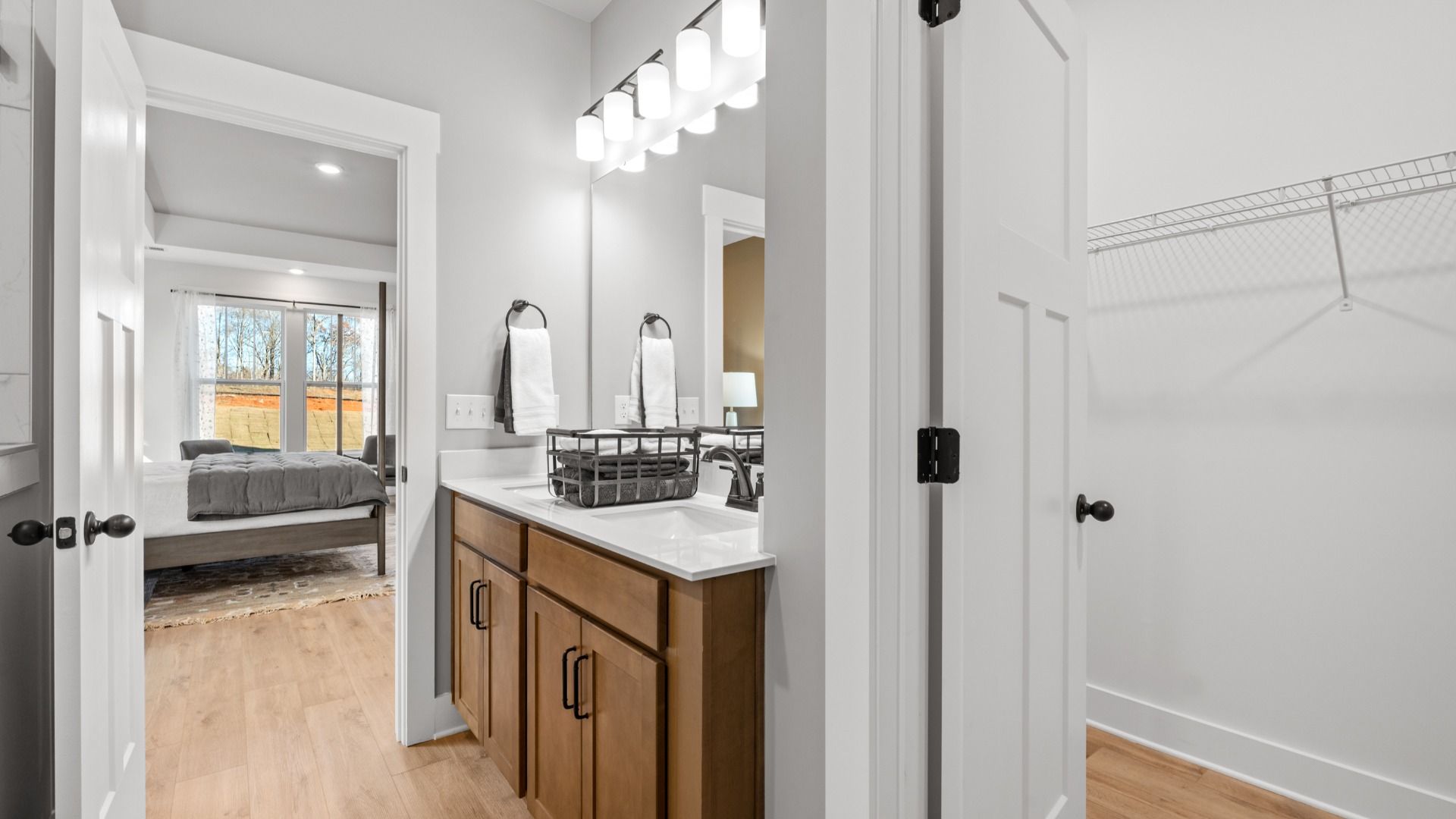 En suite primary bathroom with hardwood flooring, wood toned cabinetry, modern accents, and walk-in closet by DRB Homes