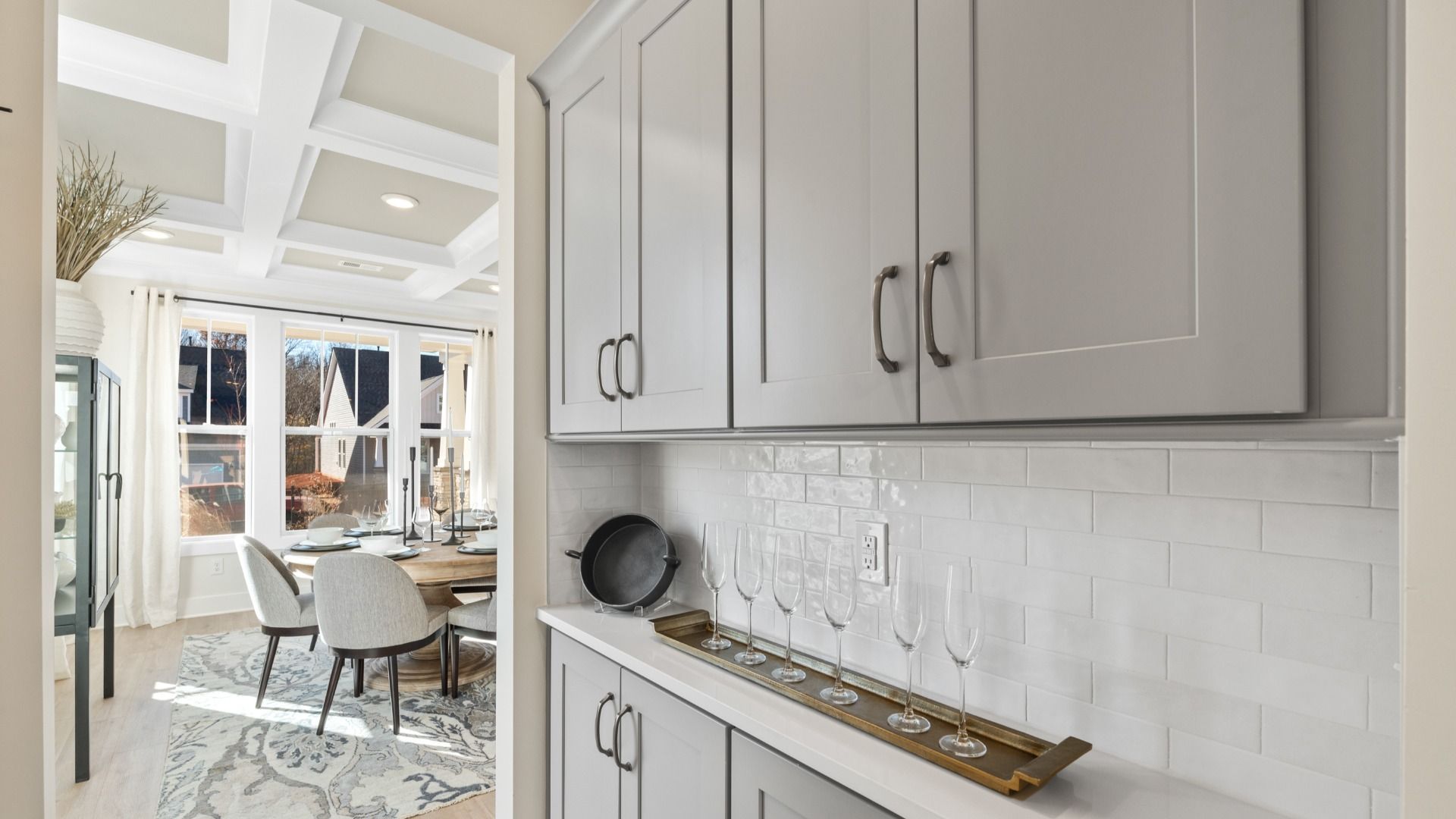 Butler's Pantry with grey cabinetry on top and bottom, white brick backsplash, and bar set up at Magnolia Park by DRB Homes