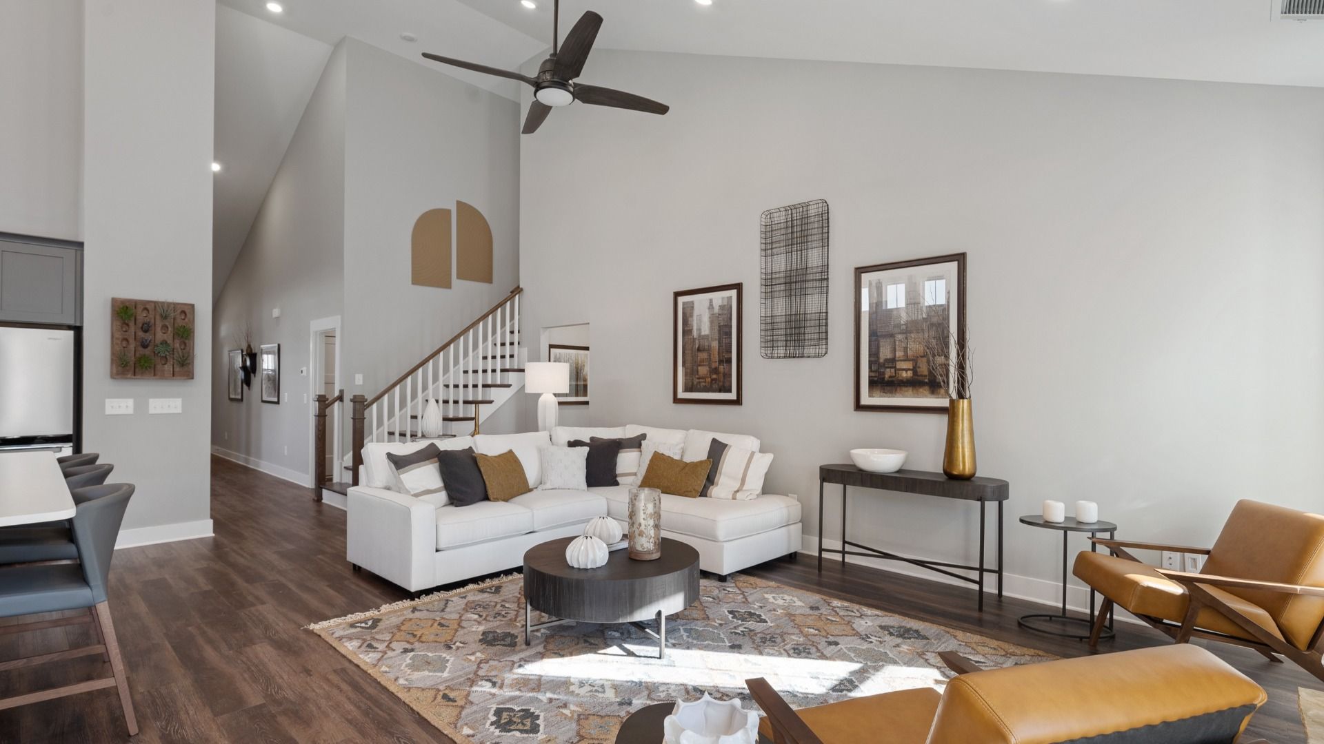Two-story ceiling family room with ceiling fan and dark hardwood flooring adjacent from kitchen at Walnut Ridge by DRB Homes