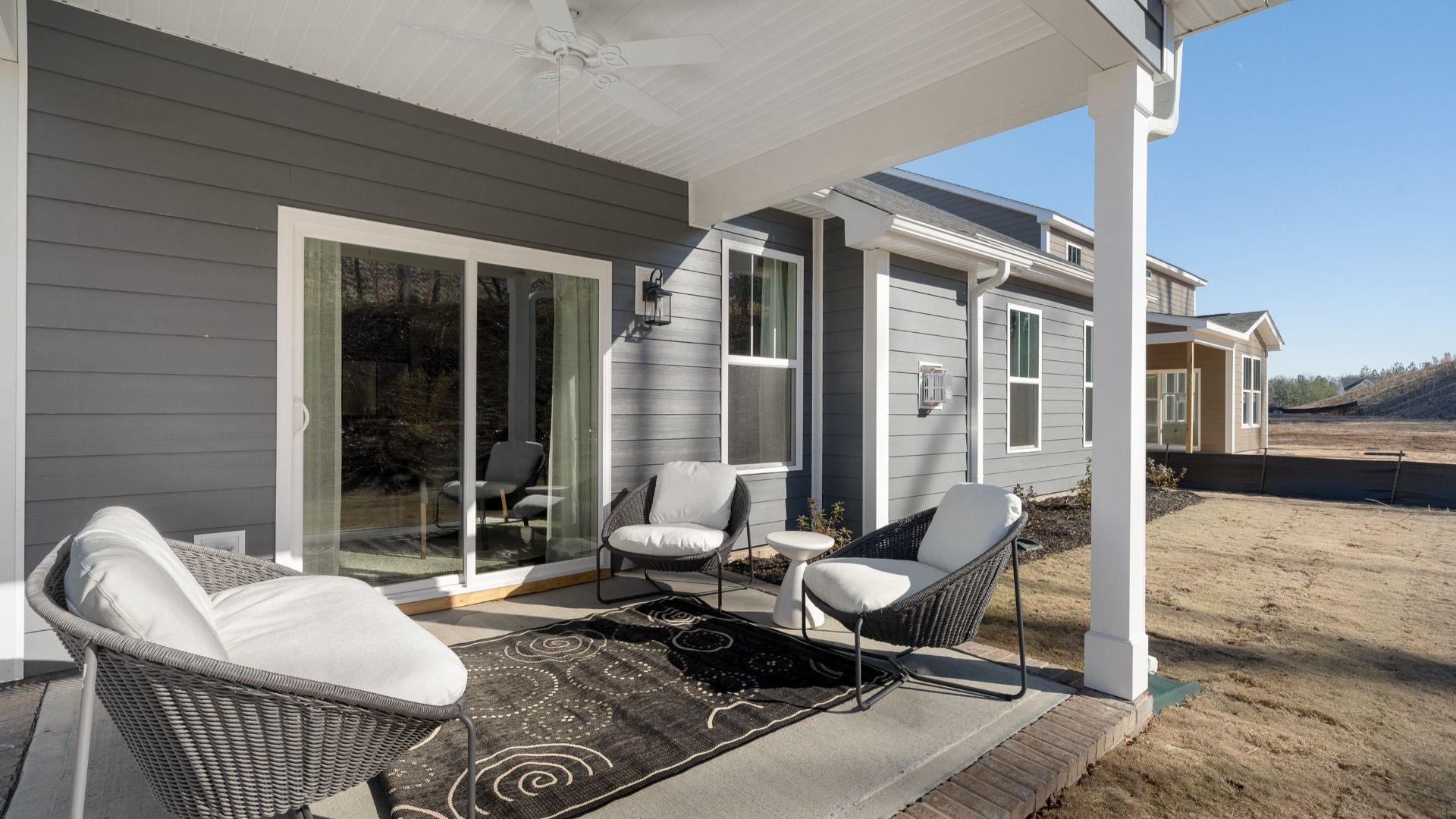 Back of gray exterior sided home with covered porch with sliding door, and ceiling fan at Walnut Ridge by DRB Homes