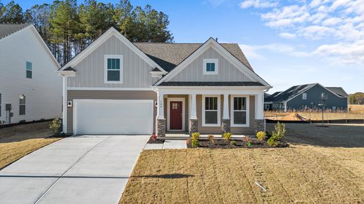 Two toned, neutral exterior home with red door, front porch, two car garage, and stone columns at DRB Homes in Greenville, SC