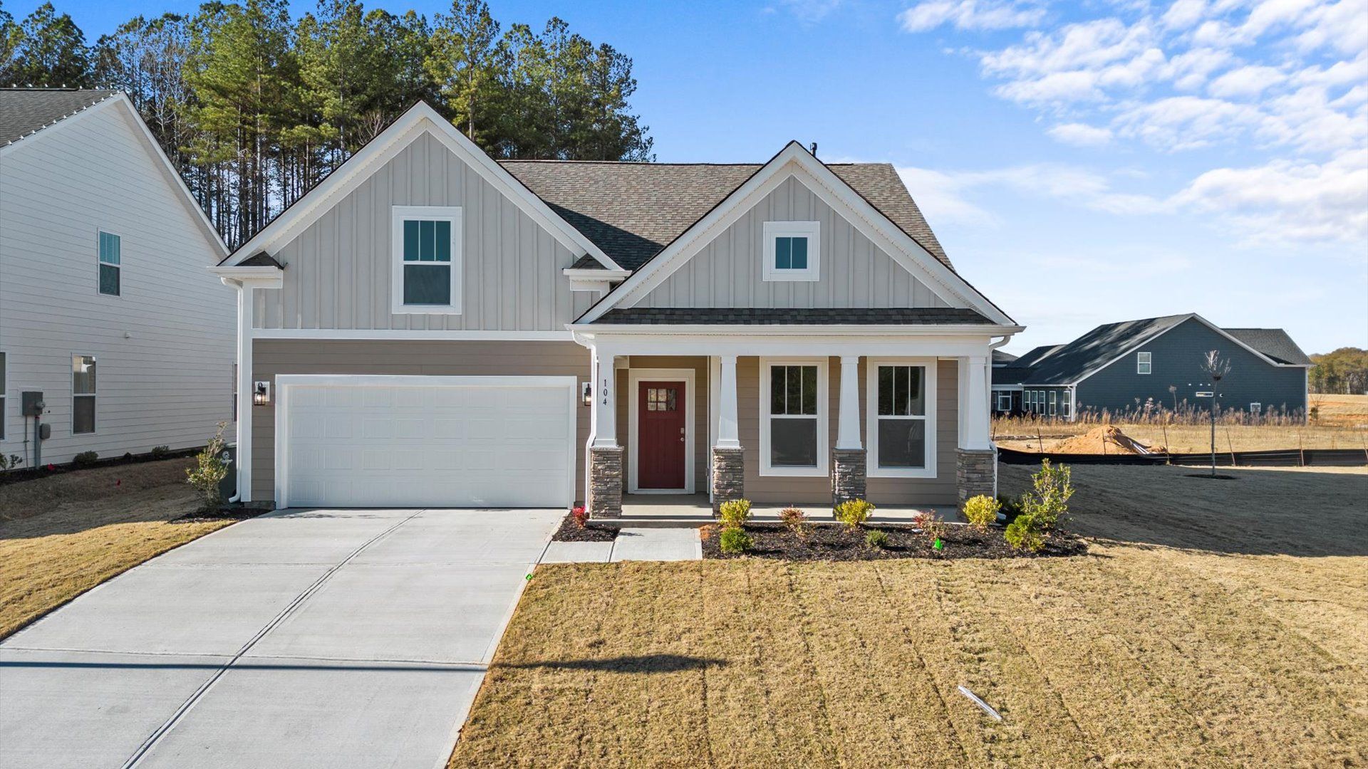 Two toned, neutral exterior home with red door, front porch, two car garage, and stone columns at DRB Homes in Greenville, SC
