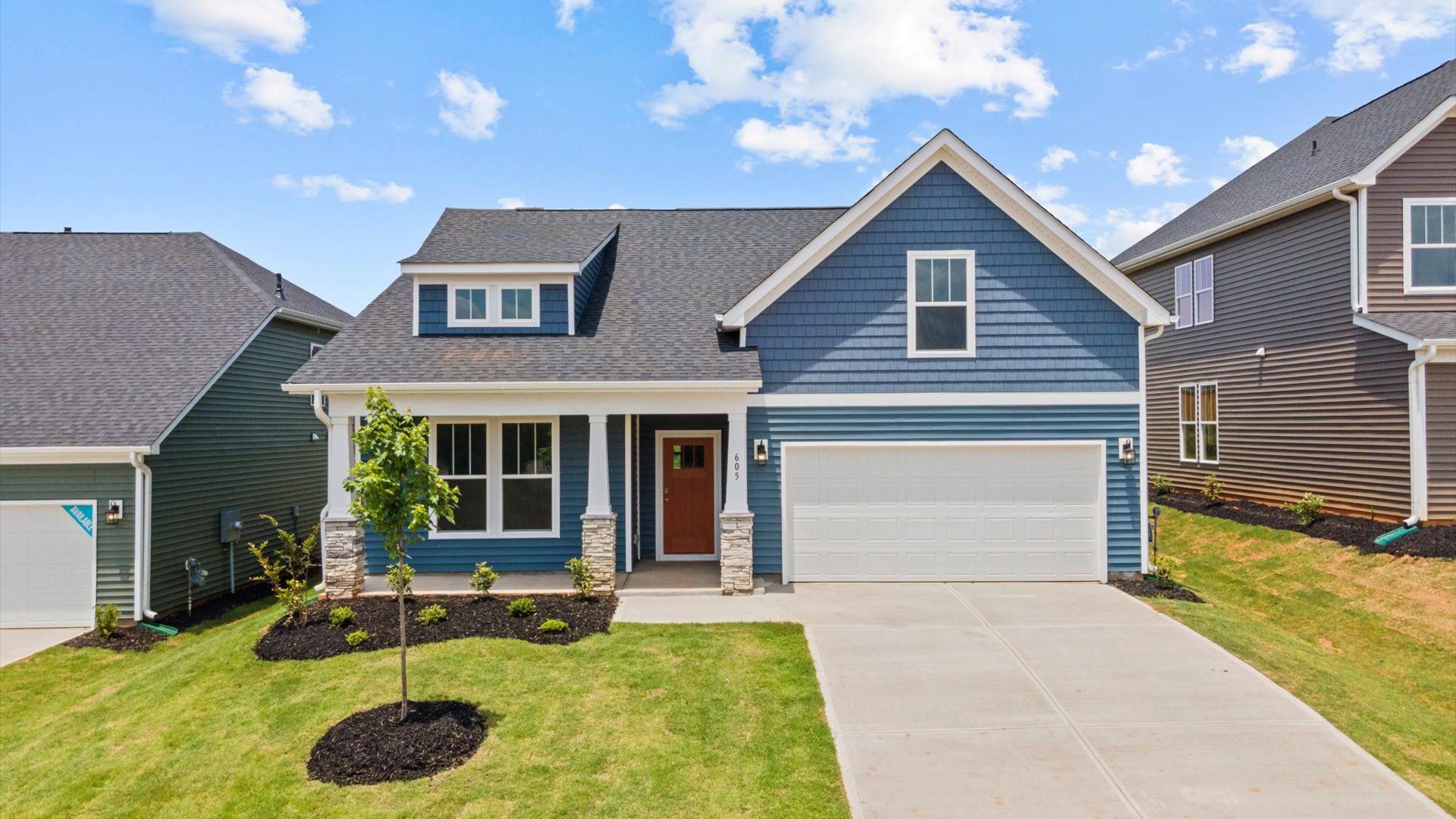 Stunning shot of dark blue exterior home with two car garage, stone columns, and front porch at Pelham Crossing by DRB Homes