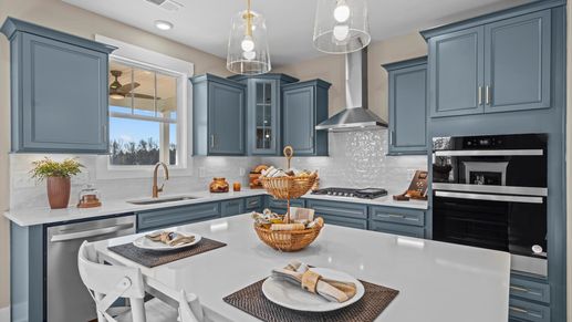 Gold accented kitchen with stunning blue cabinetry, white backsplash, and pendant lighting at Pelham Crossing by DRB Homes