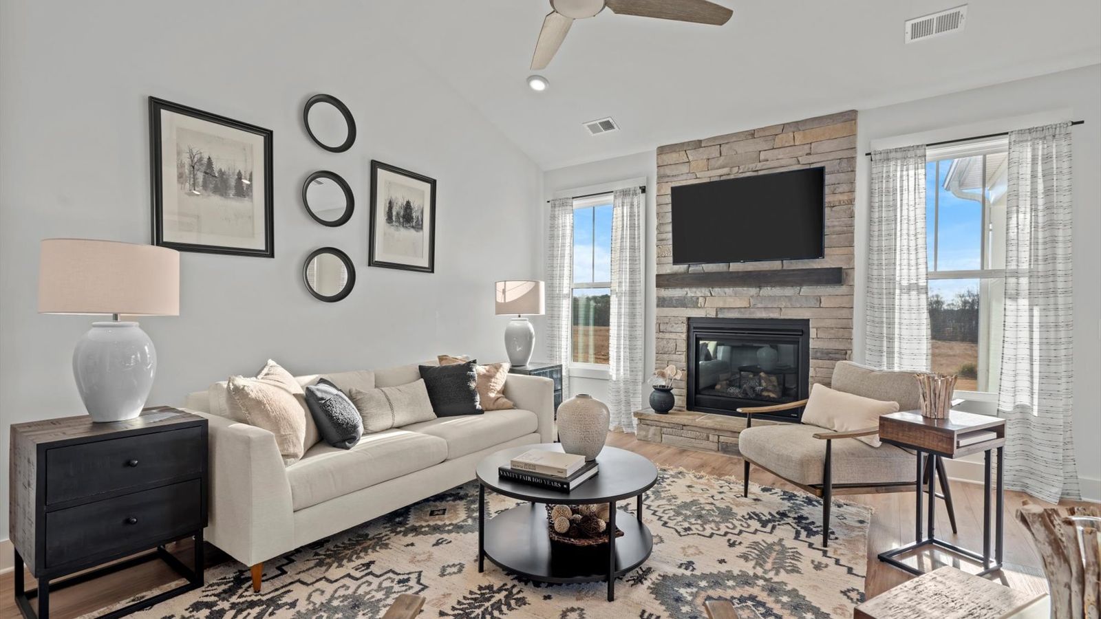 Two story ceiling family room with cozy stone fireplace, large windows, and ceiling fan at Pelham Crossing by DRB Homes