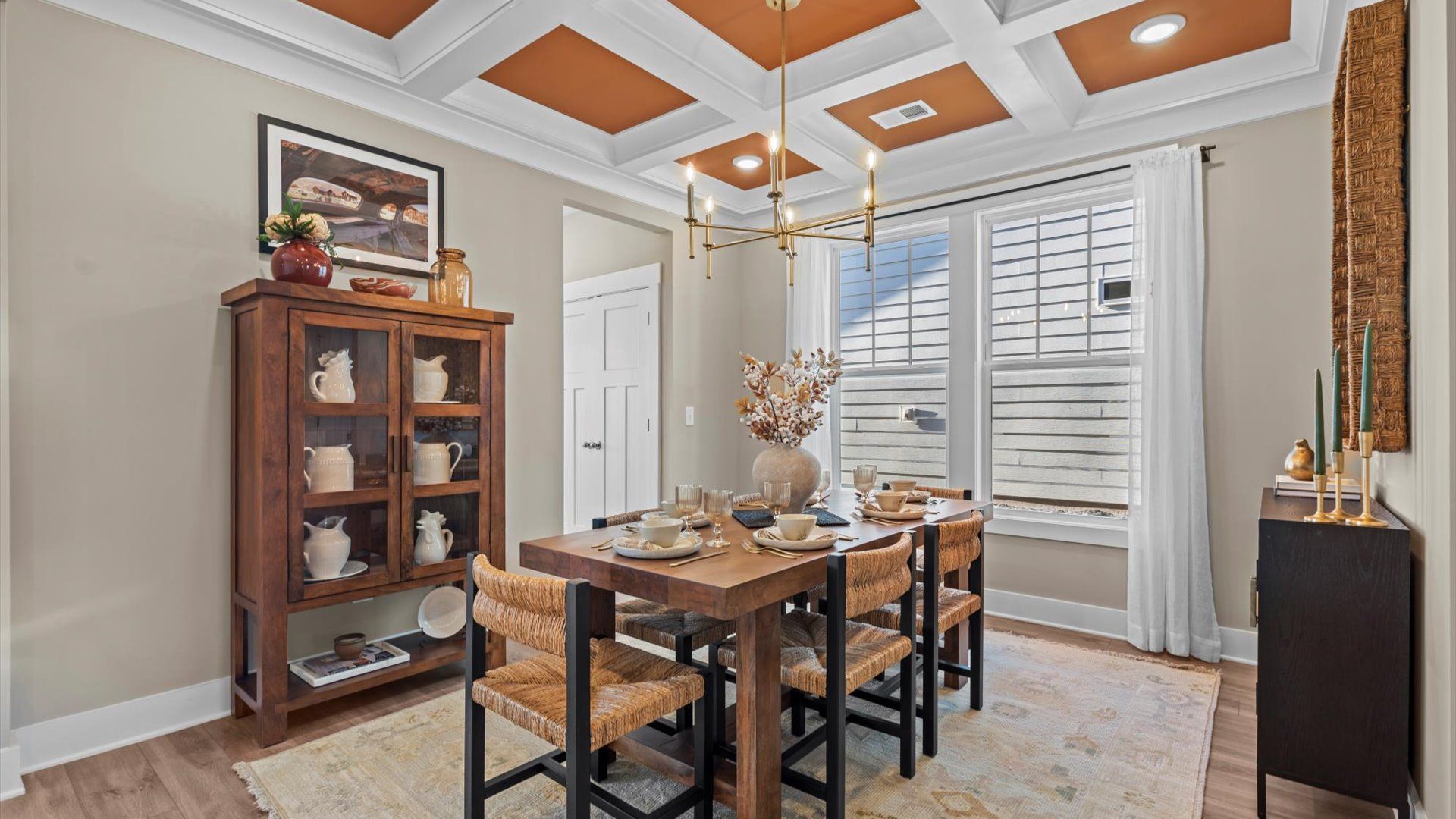 Coffered ceiling dining room with orange accent, stunning gold chandelier, & large bay window at Pelham Crossing by DRB Homes
