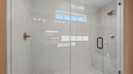 Stunning marble tiled walk-in frameless shower with bench seat and gold accents at Pelham Crossing in Greenville, SC
