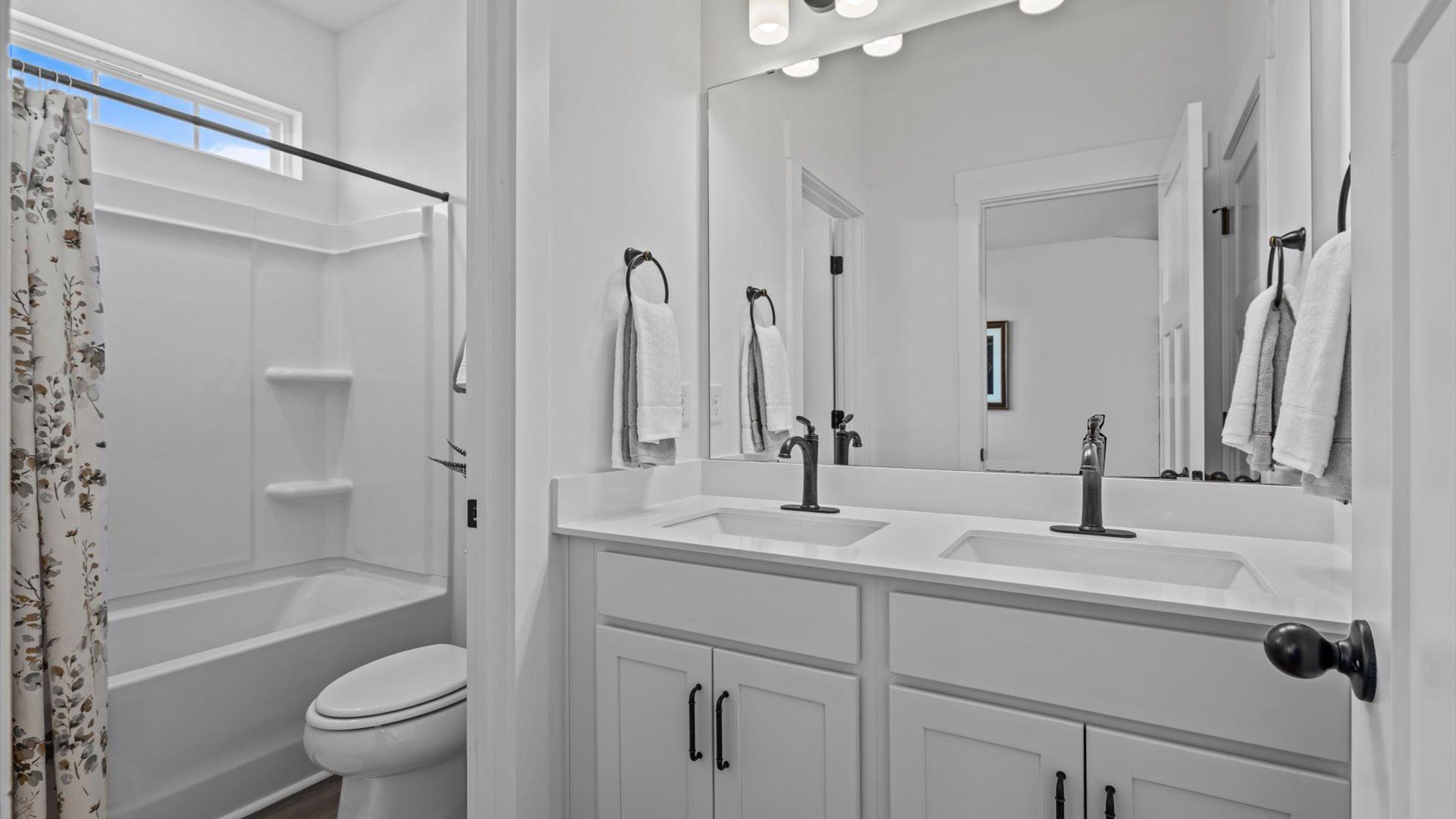Double sink vanity with white cabinetry and black accents in secondary bathroom at Pinebrook by DRB Homes in Woodruff, SC