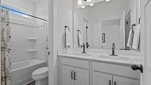 Double sink vanity with white cabinetry and black accents in secondary bathroom at Pinebrook by DRB Homes in Woodruff, SC