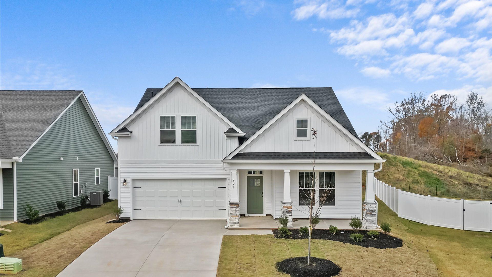 Single-family home with all white vinyl siding, a two-car garage, and beautiful landscaping at Harrier Point in Woodruff, SC
