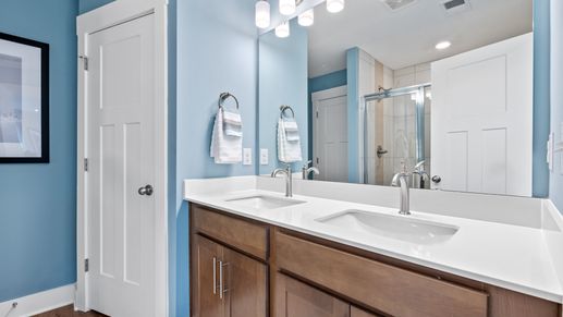 En suite primary bathroom with double sink vanity & tiled shower with silver accents at Hickory Heights