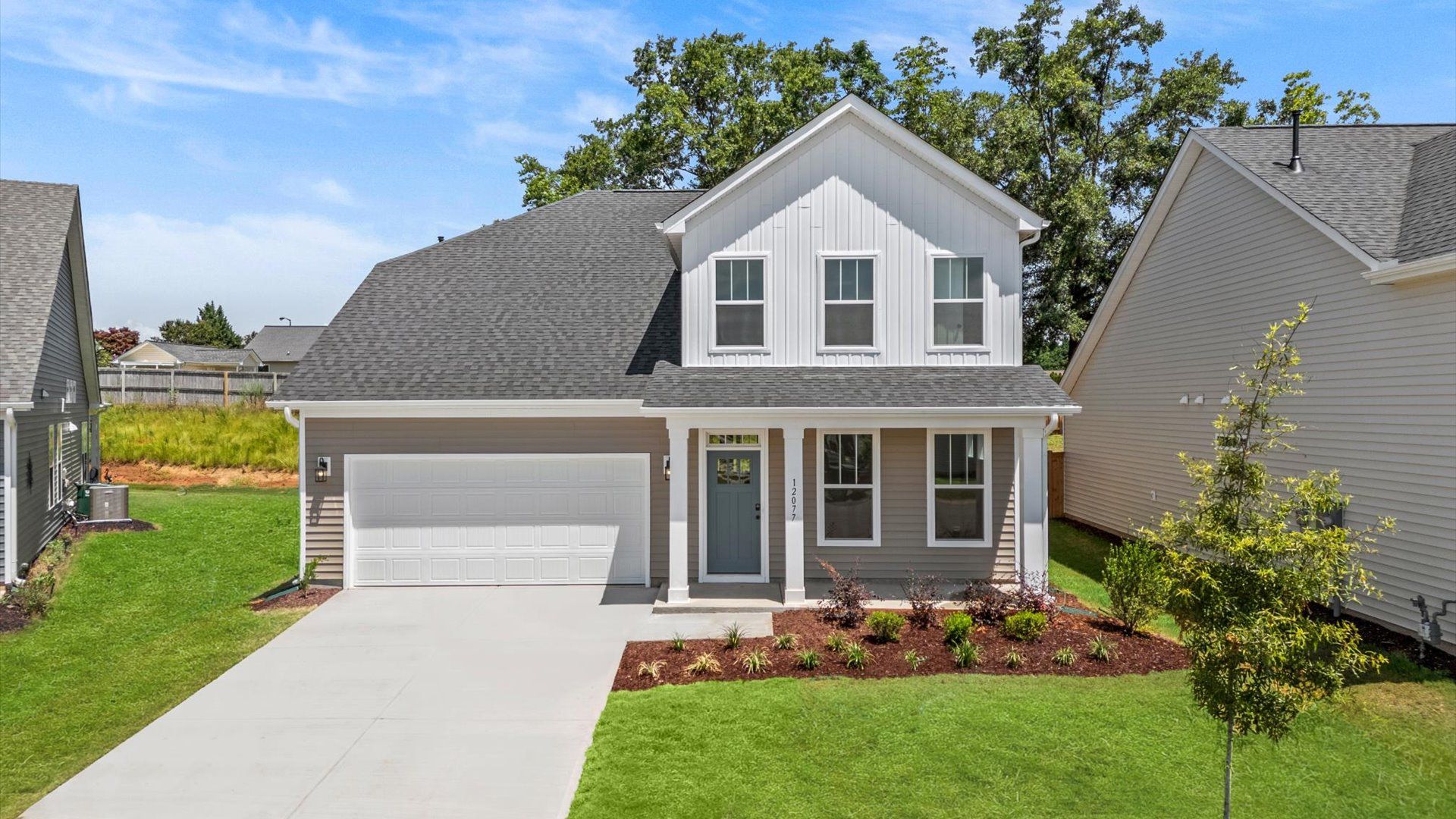 Beige and white siding two-story home with blue door, covered porch, two-car driveway and two-car garage in Woodruff, SC