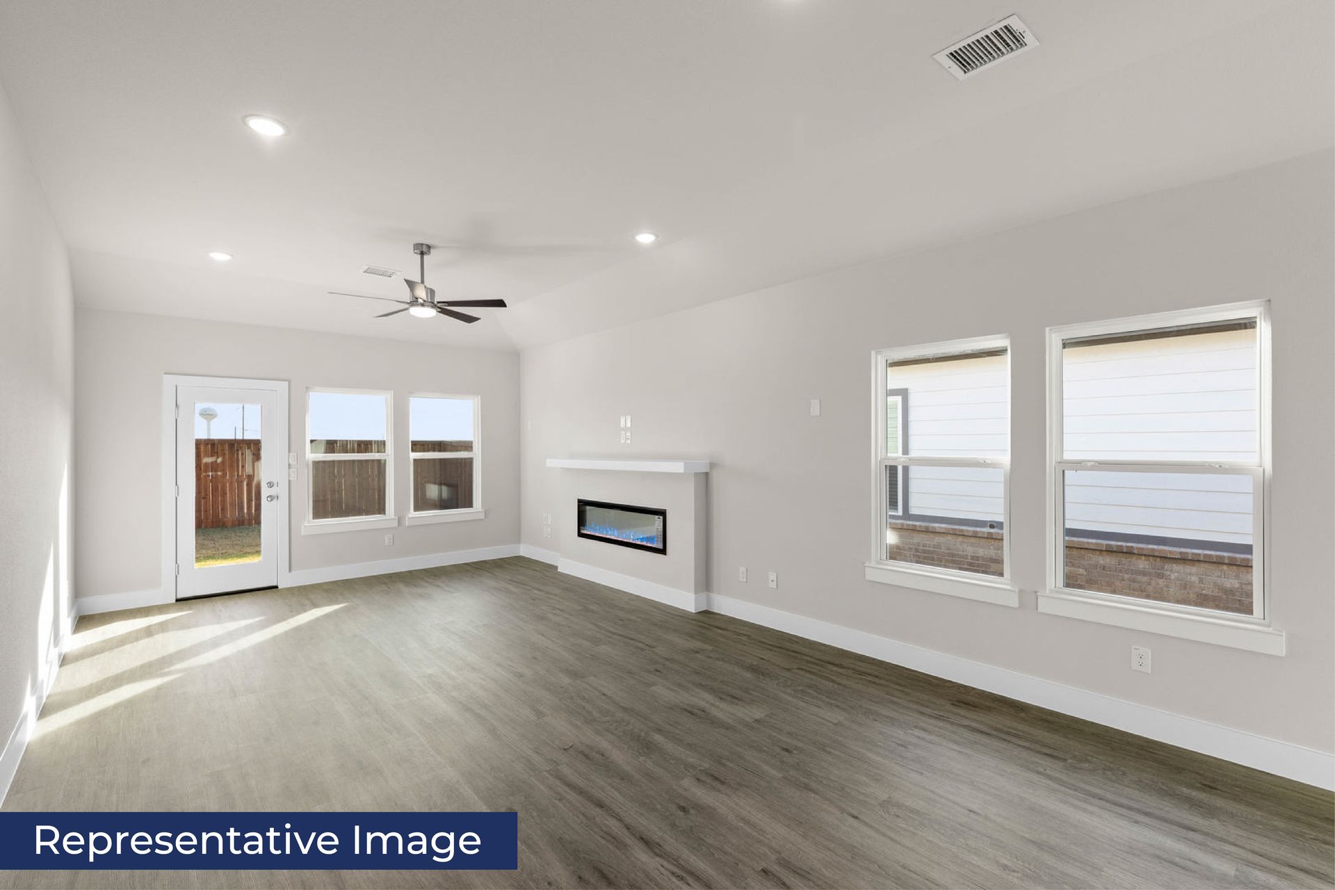 Spacious living room with wood flooring, ceiling fan, and large windows.