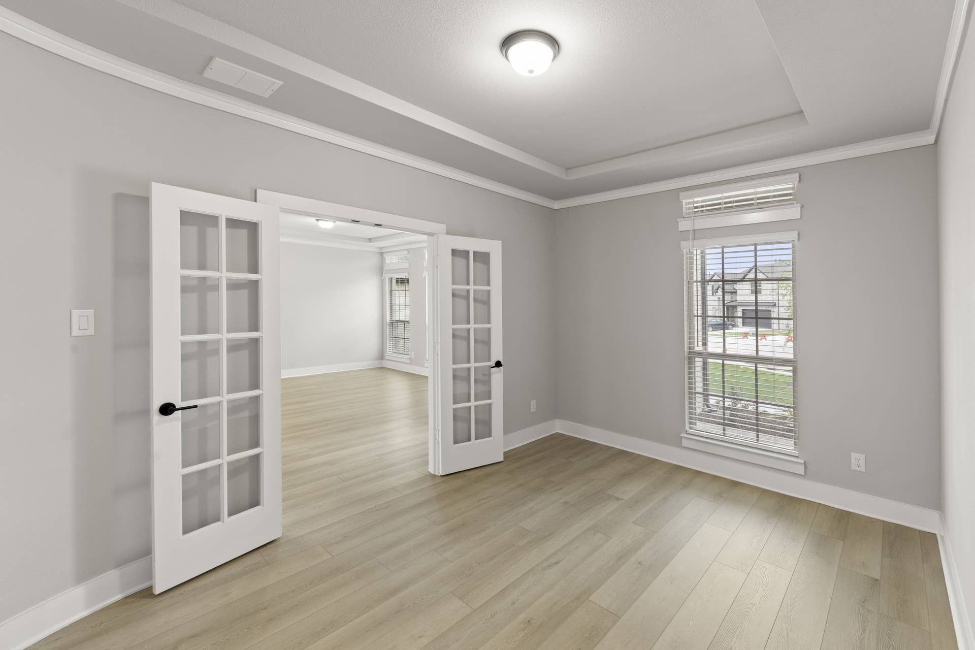 Bright study room with French doors and large window, featuring light wood flooring.