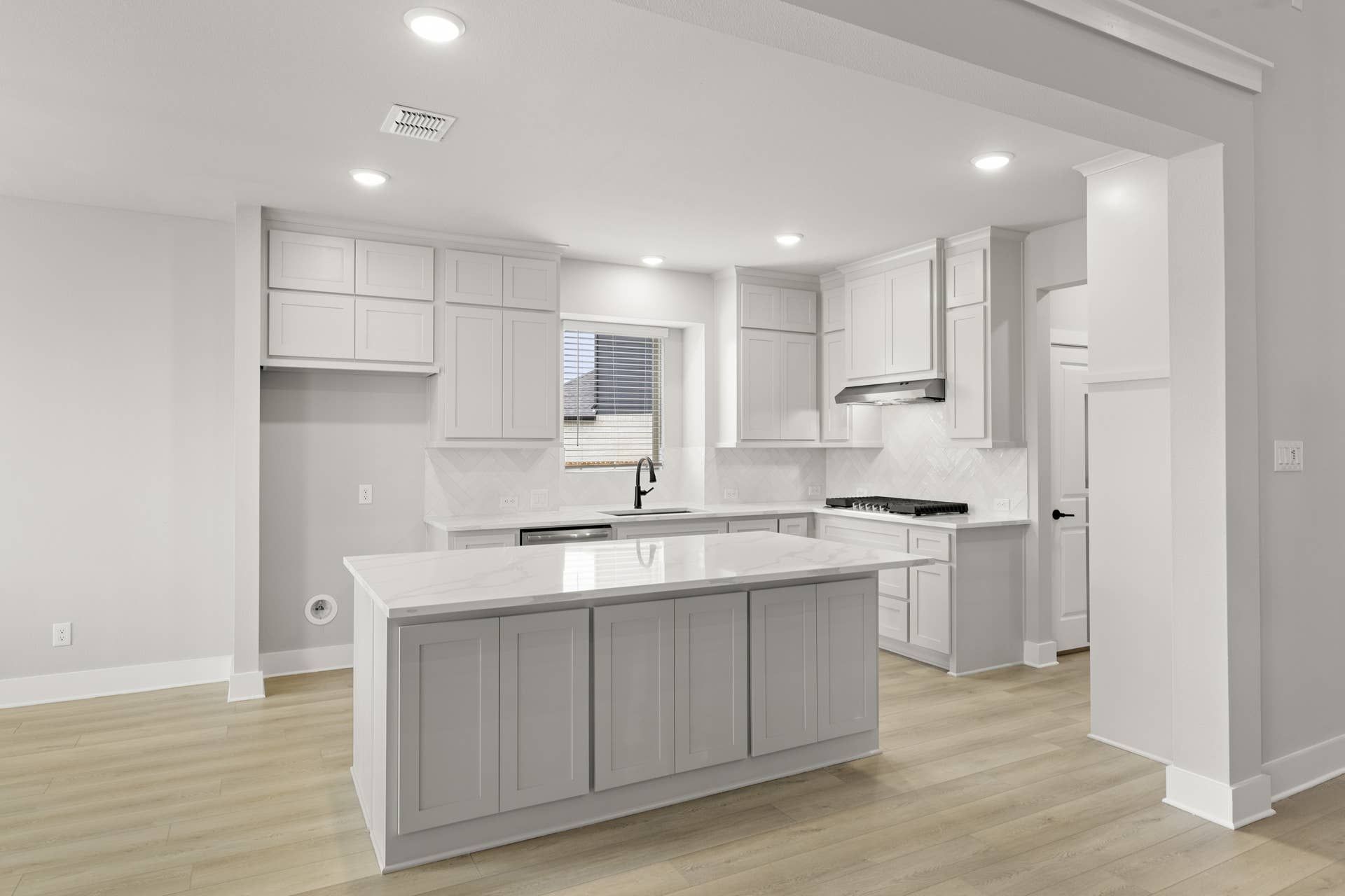 Modern kitchen with white cabinetry and center island, featuring recessed lighting.