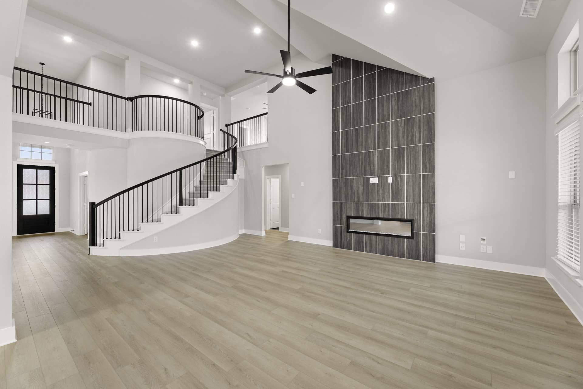 Spacious modern living room with curved staircase and sleek fireplace feature wall.