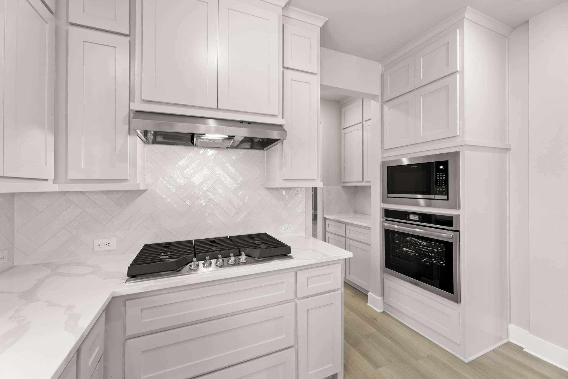 Modern kitchen with white cabinets, herringbone backsplash, and built-in appliances.