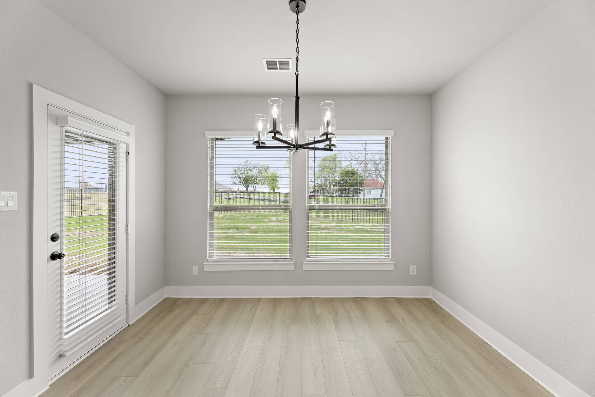 Bright dining nook with modern chandelier and large windows overlooking a green lawn.