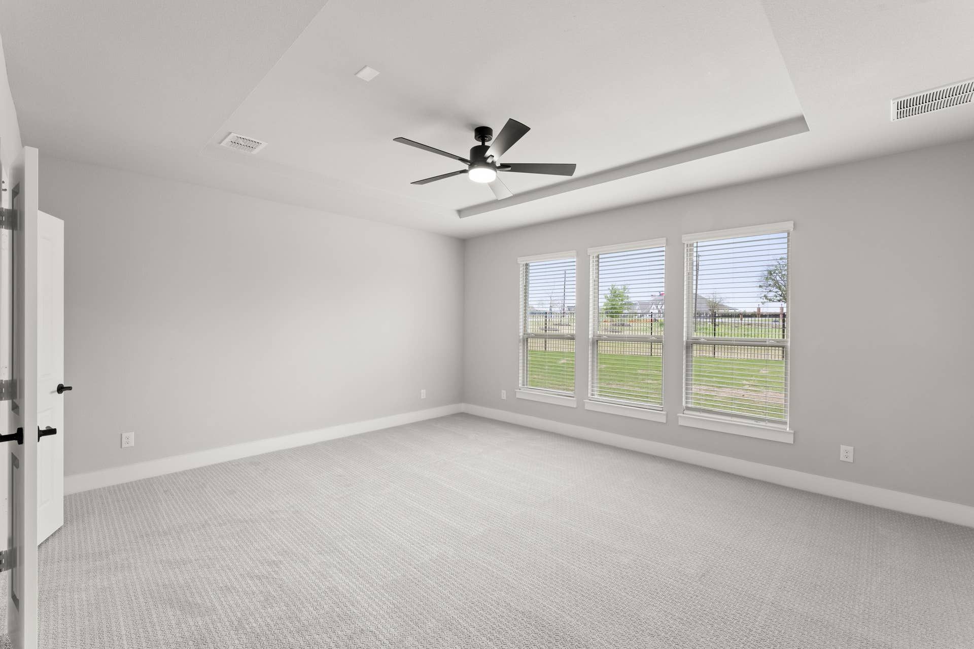 Spacious bedroom with ceiling fan and large windows overlooking a green yard.