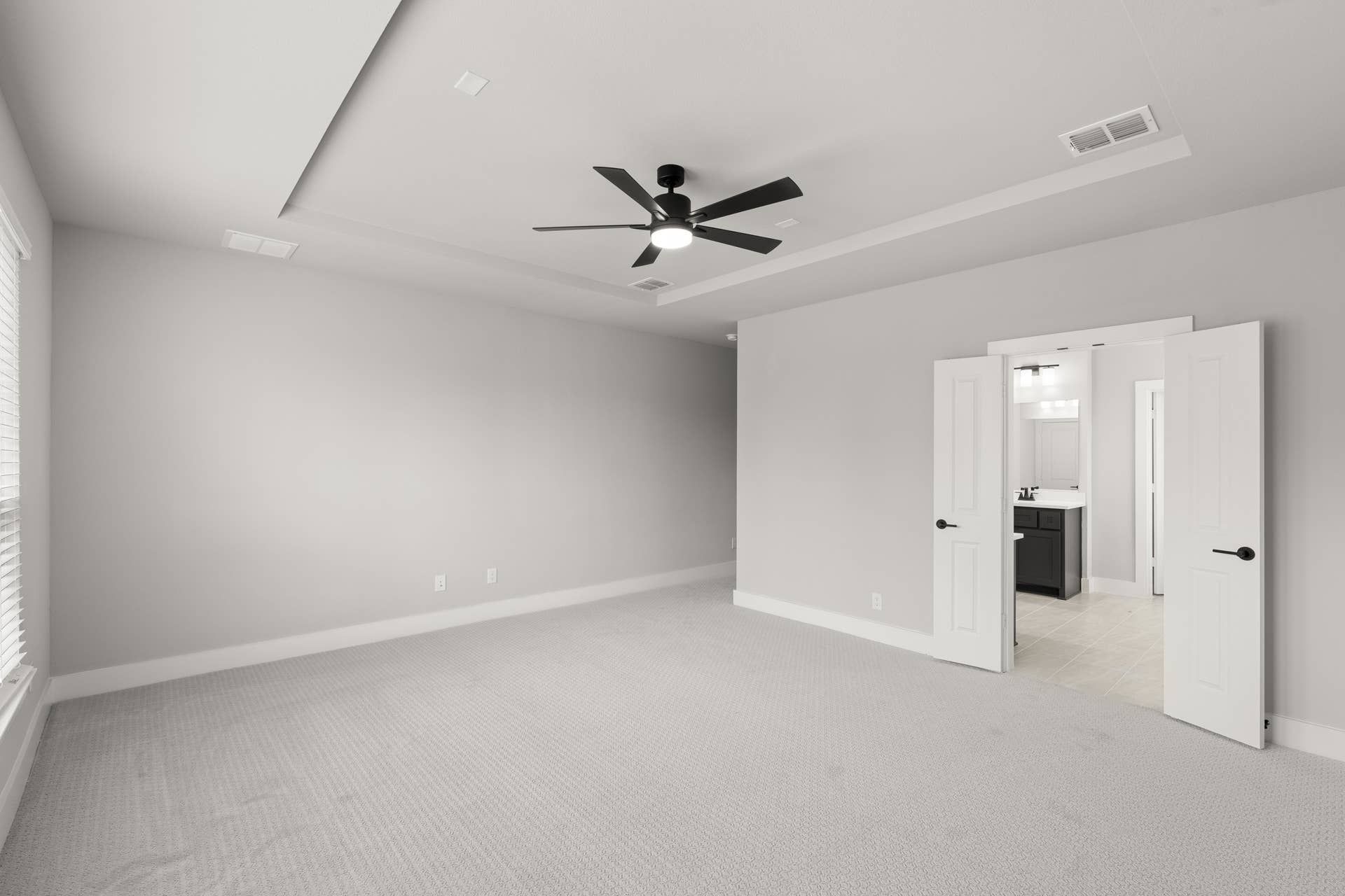 Spacious primary bedroom with ceiling fan and en-suite bathroom entrance.