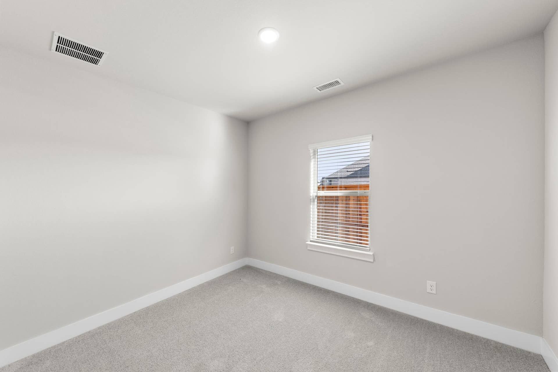 Bright bedroom with neutral carpet and single window with blinds.