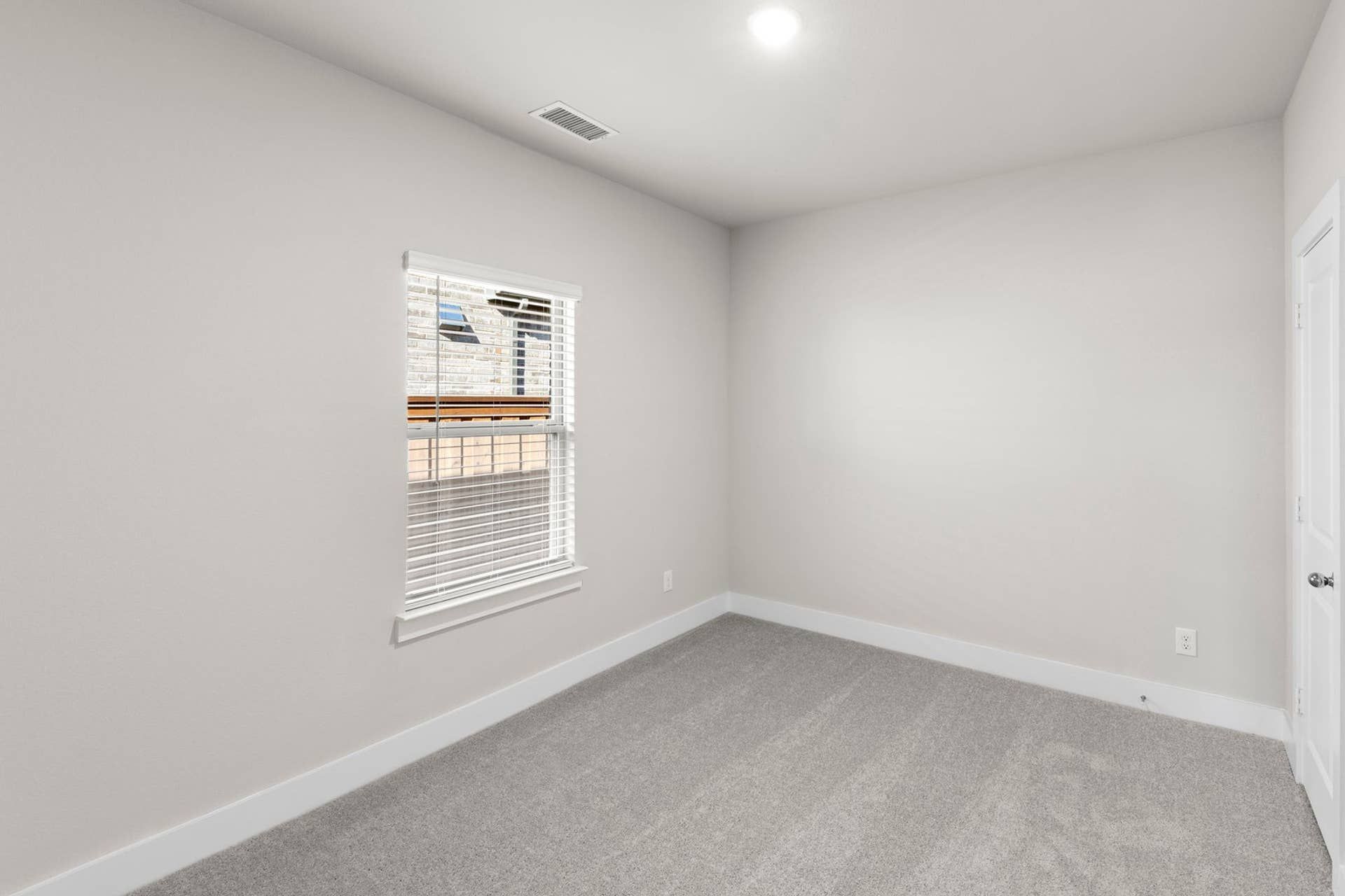 Bright bedroom with gray carpet and a single window.
