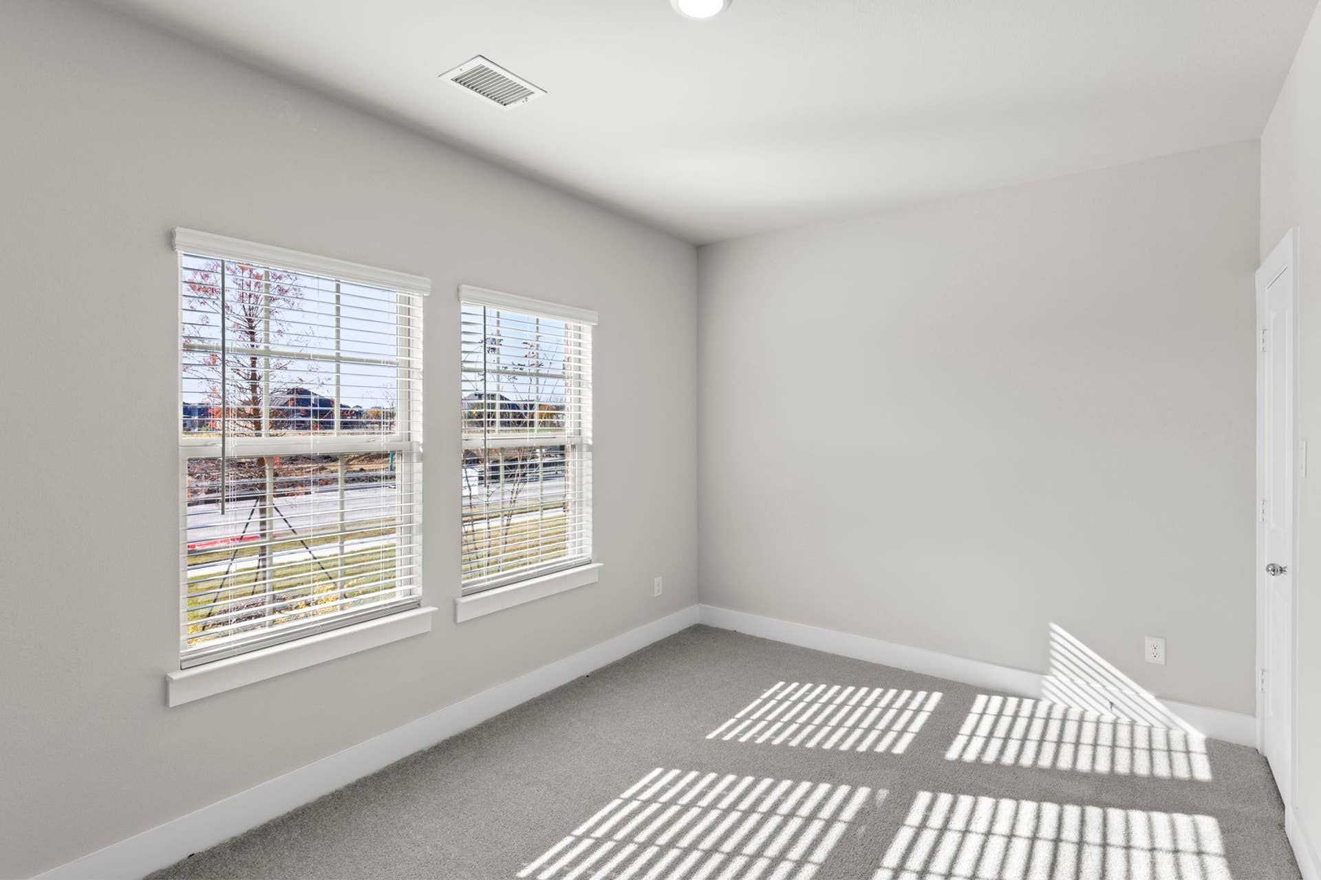 Bright bedroom with large windows and carpeted floor.
