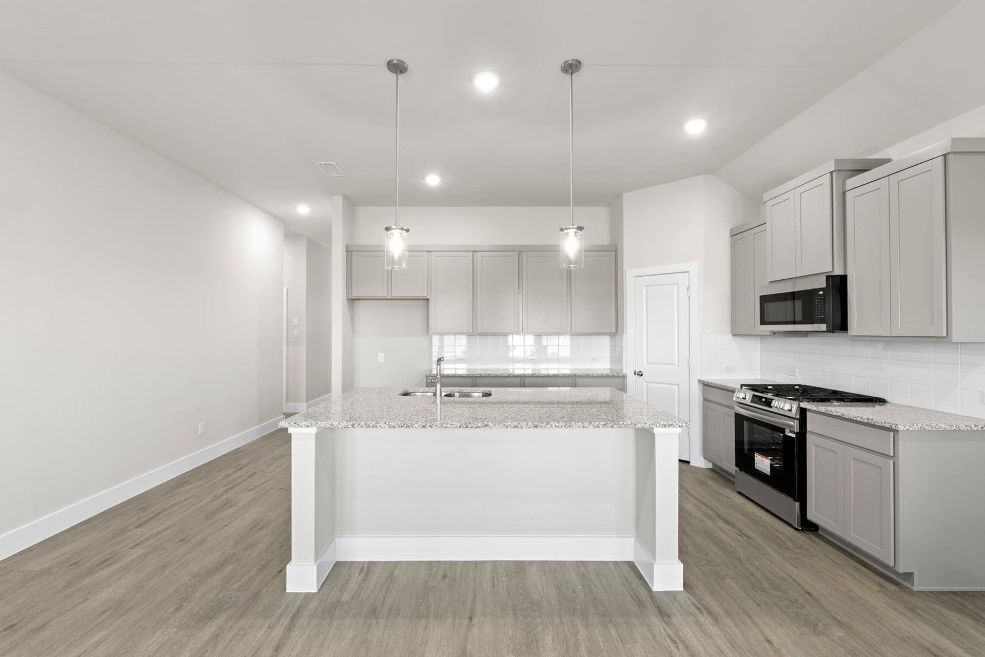 Modern kitchen with granite island, pendant lighting, and stainless steel appliances.