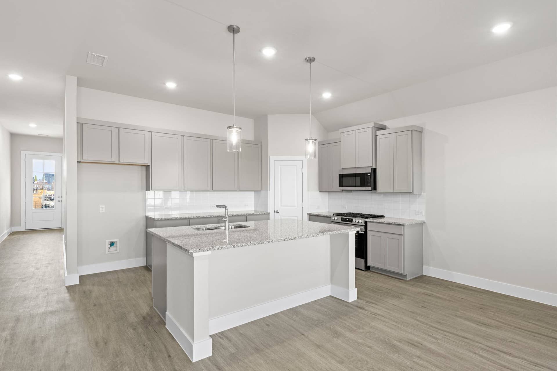 Modern kitchen with gray cabinets, granite countertops, and pendant lighting.